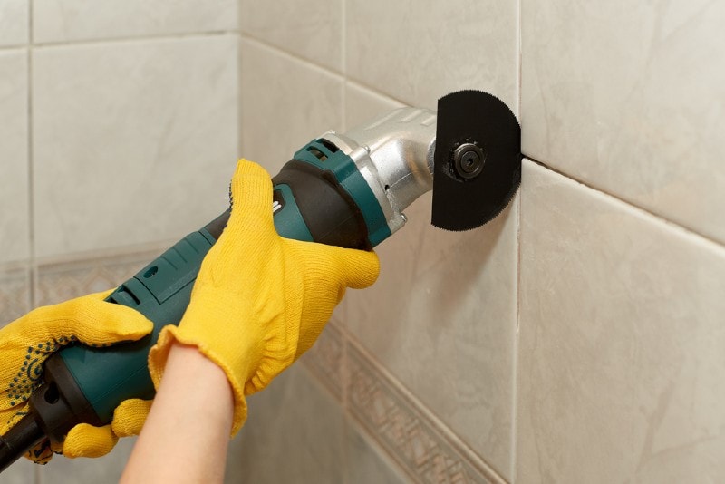 man using multi tool to remove old grout from tiles