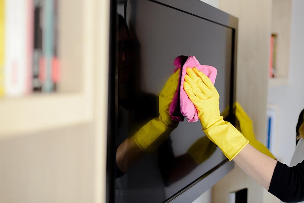 woman wearing gloves wiping the tv