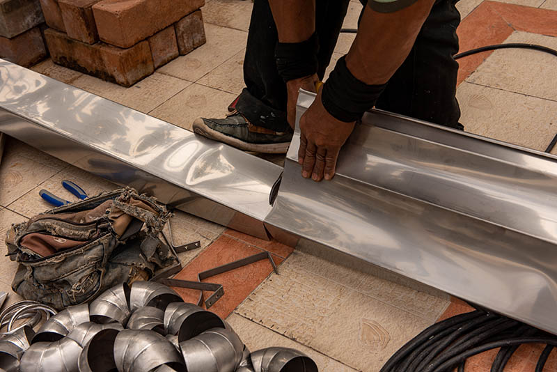 Hands of skilled workers using scissors cutting stainless steel rain gutters