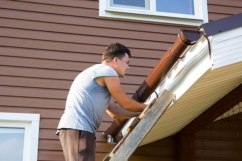 Man attaches gutter on the roof of the porch
