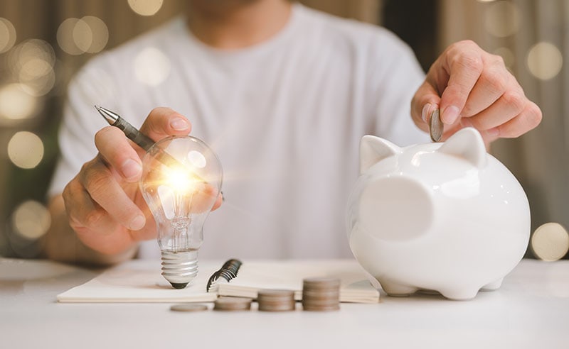 Man hand holding lightbulb and putting coin in to the piggy bank idea saving energy