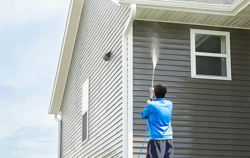 Man using a high-pressure nozzle spray to clean the house