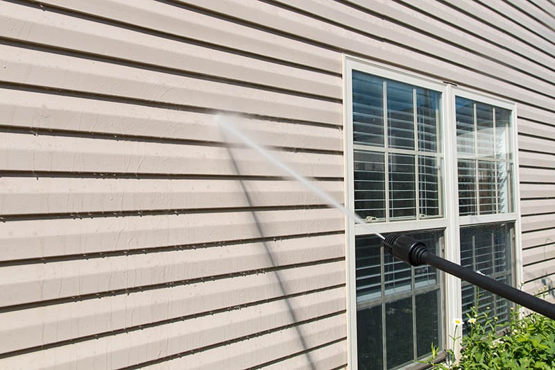 Power washing. House wall vinyl siding cleaning with high pressure water jet