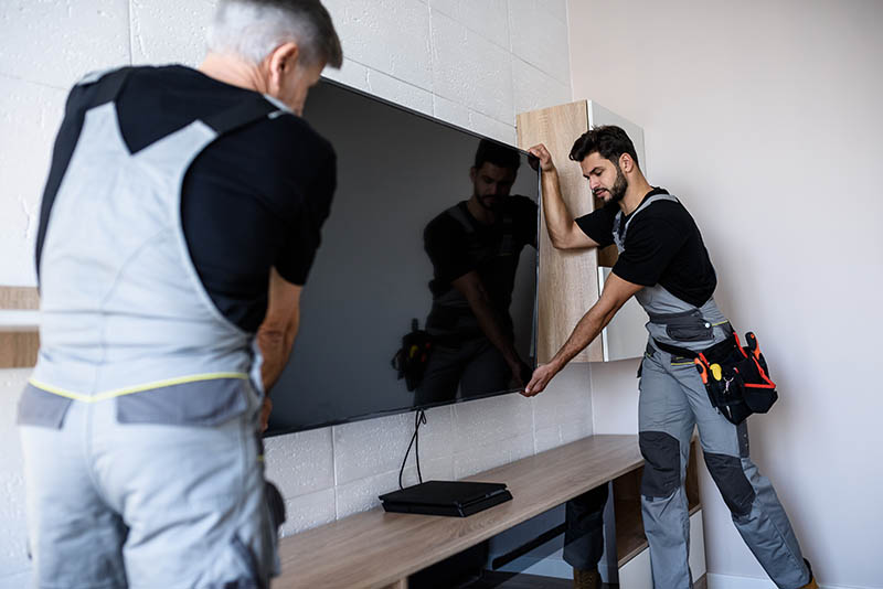 Two professional technicians, workers in uniform installing television on the wall indoors