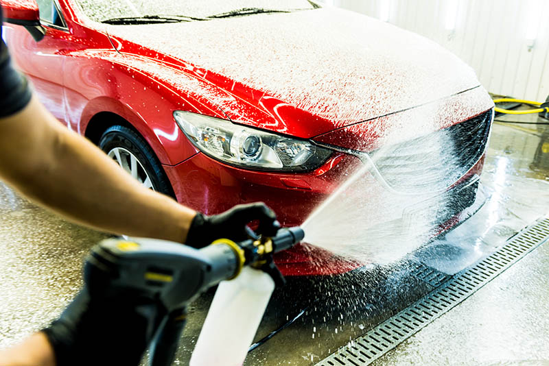 Worker washing car with active foam on a car wash