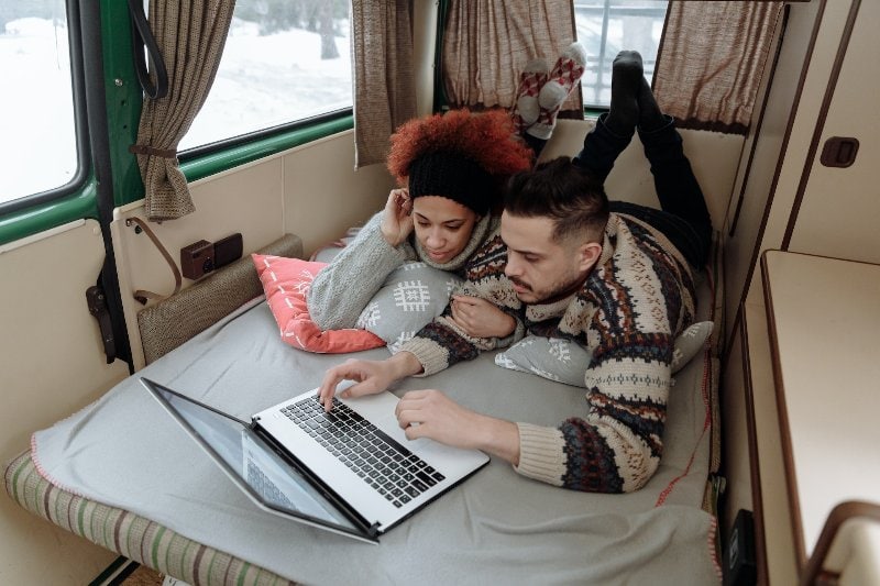 a couple using a laptop and lying on a bed inside an rv