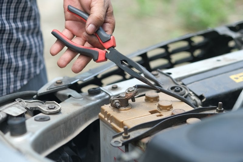 a person holding pliers over a car battery