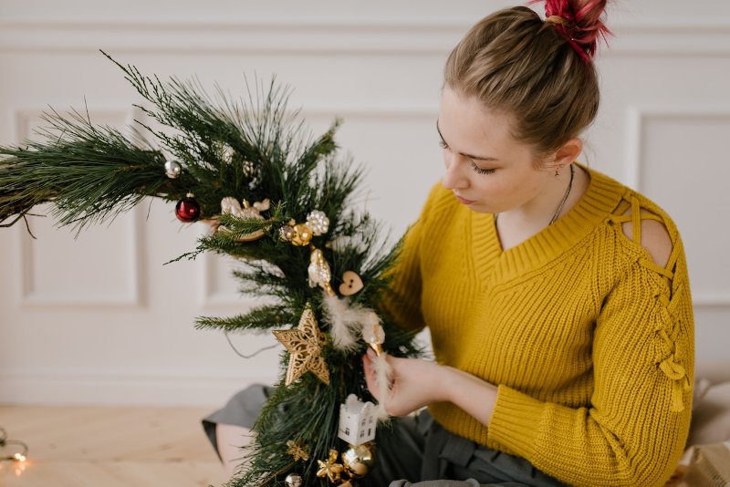 a woman in yellow sweater making a christmas wreath decor