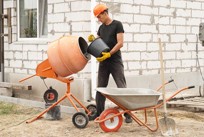 construction worker with a bucket in his hands loads a concrete mixer