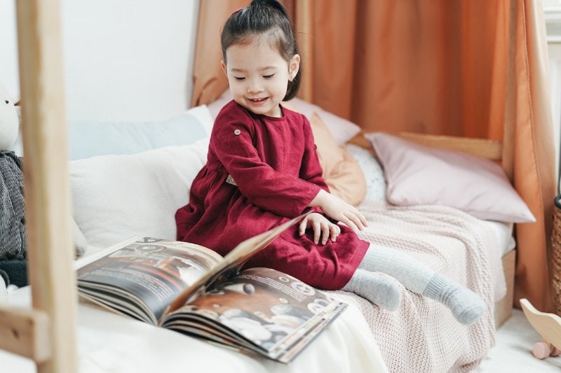 little girl sitting on a small bed reading
