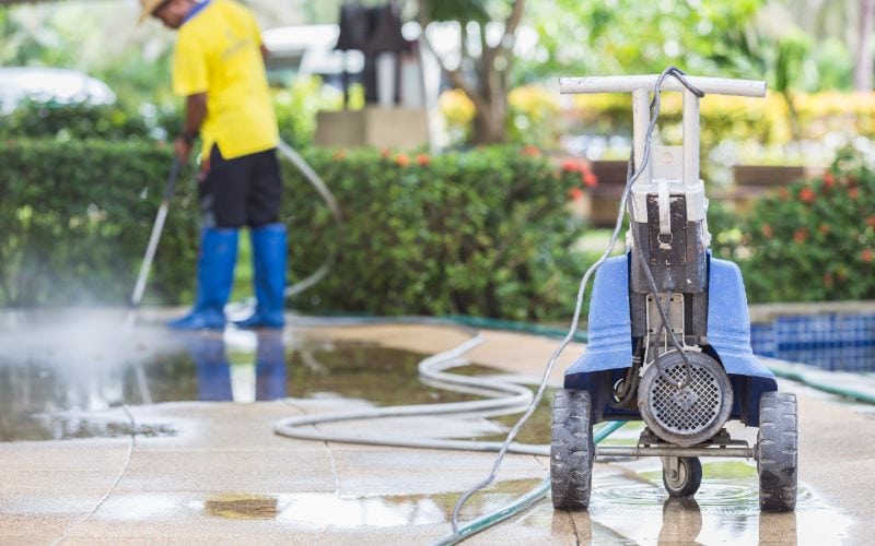man using pressure washer to clean outdoor floor