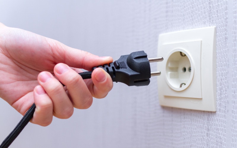 person plugging in a black plug into wall power outlet socket