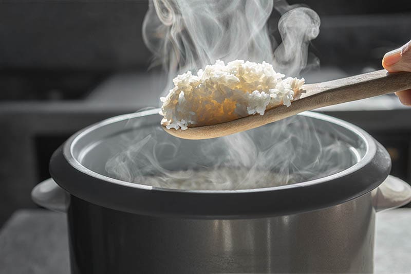 scooping rice from an electric rice cooker using a wooden ladle