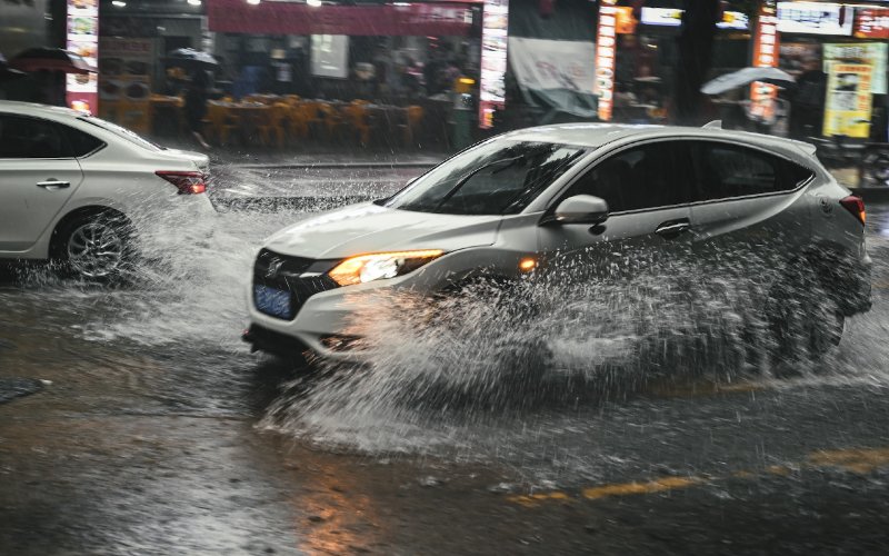 silver car plowing through flood in the rain