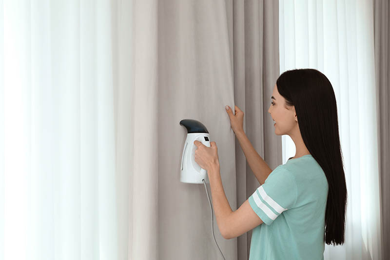 woman steaming curtain near window