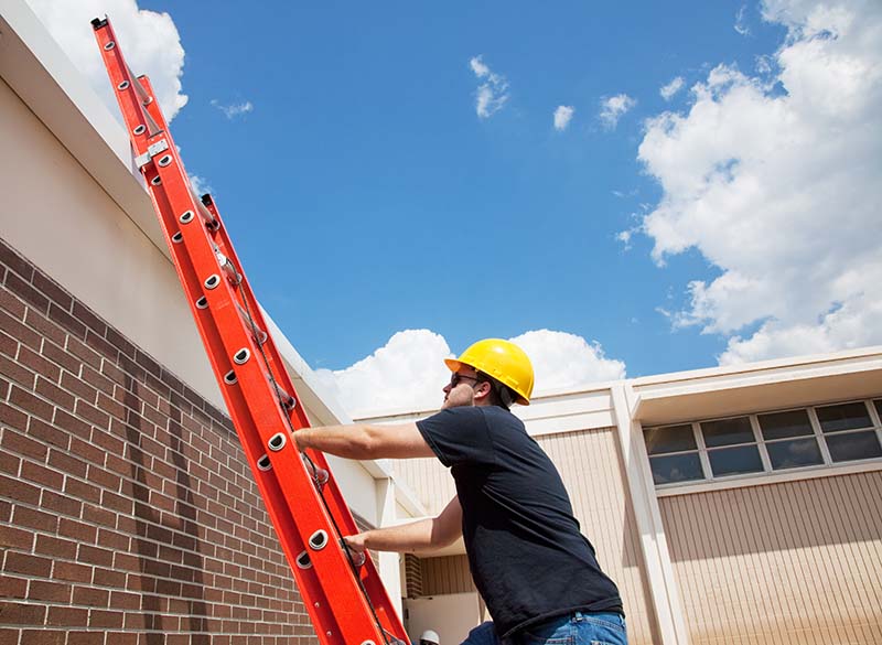 Construction worker climbing up to the roof of a building with an extension ladder