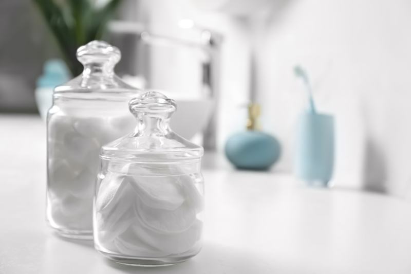 Cotton balls and pads on a glass jar on a white table in the bathroom