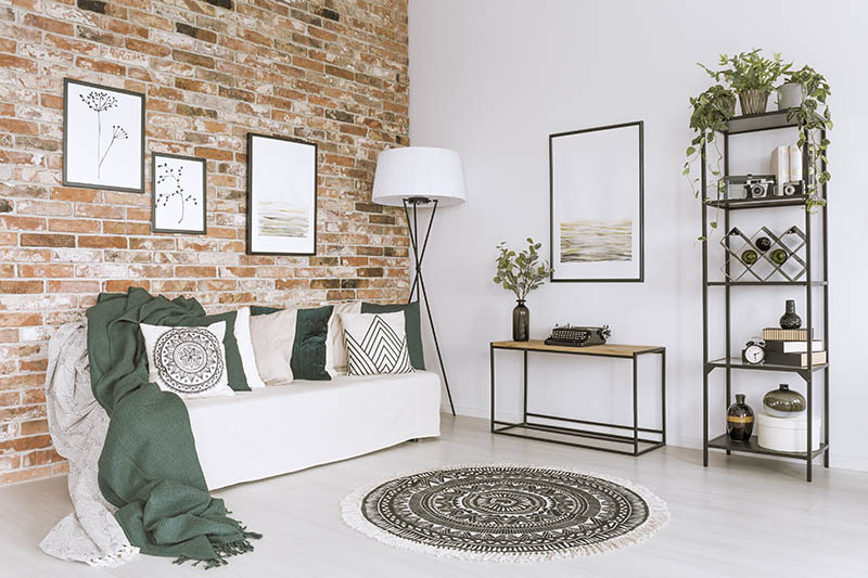 Cushions and blankets on white sofa in cozy living room with pictures on brick wall