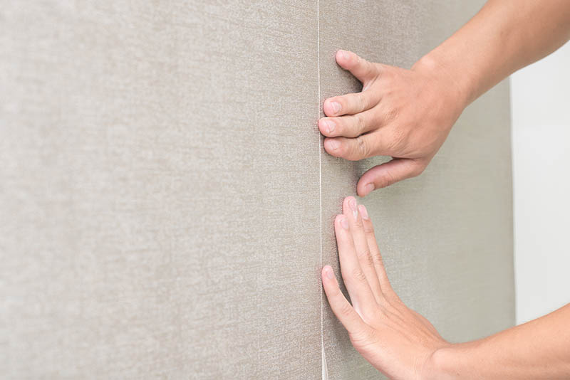Handyman putting up wallpaper on the wall
