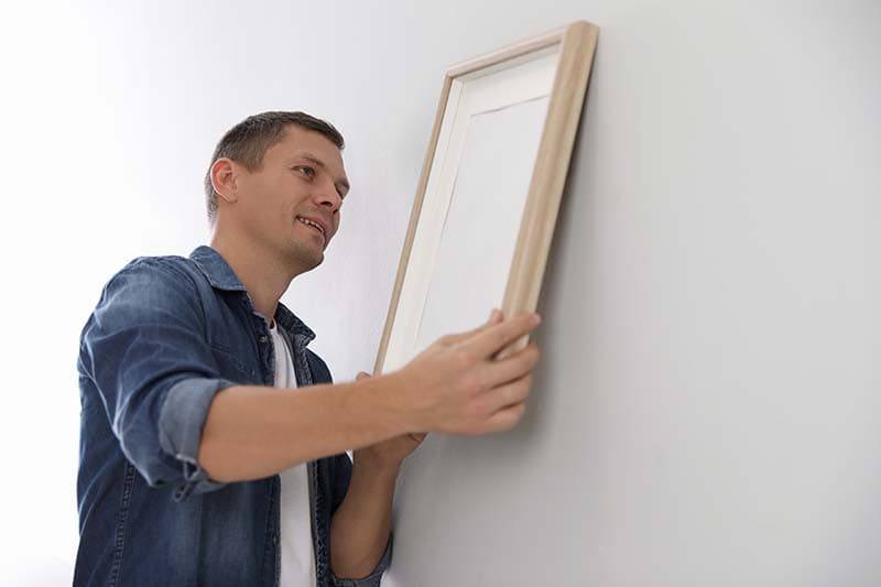 Man hanging picture on white wall indoors