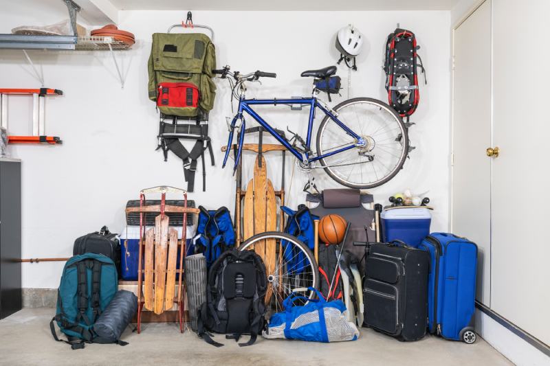 Sports and travel gear and equipment in piles in corner of messy suburban garage
