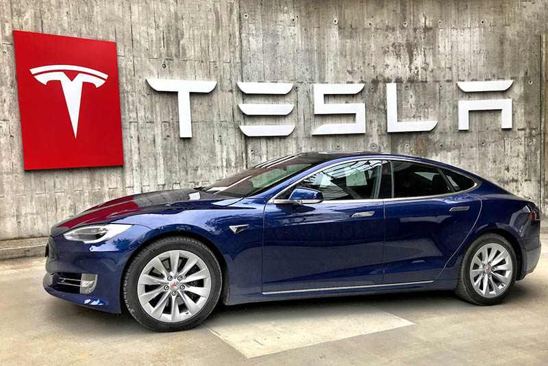 blue tesla card in front of tesla building