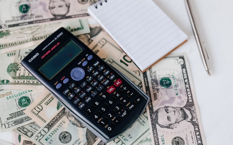 calculator and notepad on top of american currency
