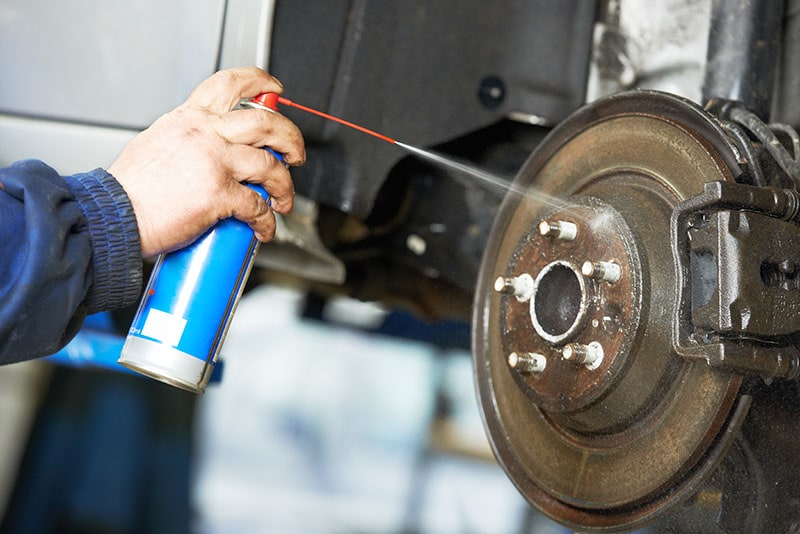 car mechanic cleaning car wheel brake disk from rust corrosion at automobile repair service station