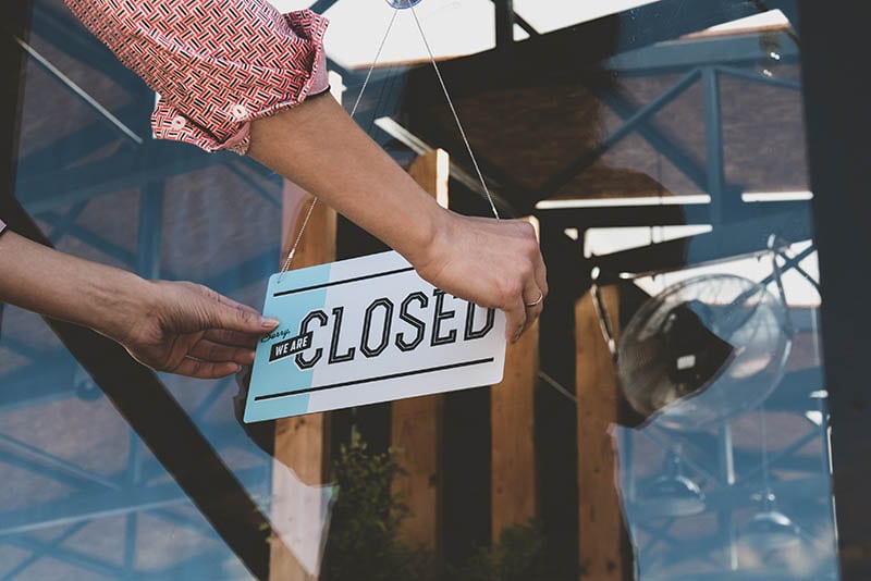 female turning sign from open to closed on the entrance door of his small cafe