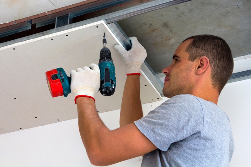 man fixing the drywall to the ceiling metal frame