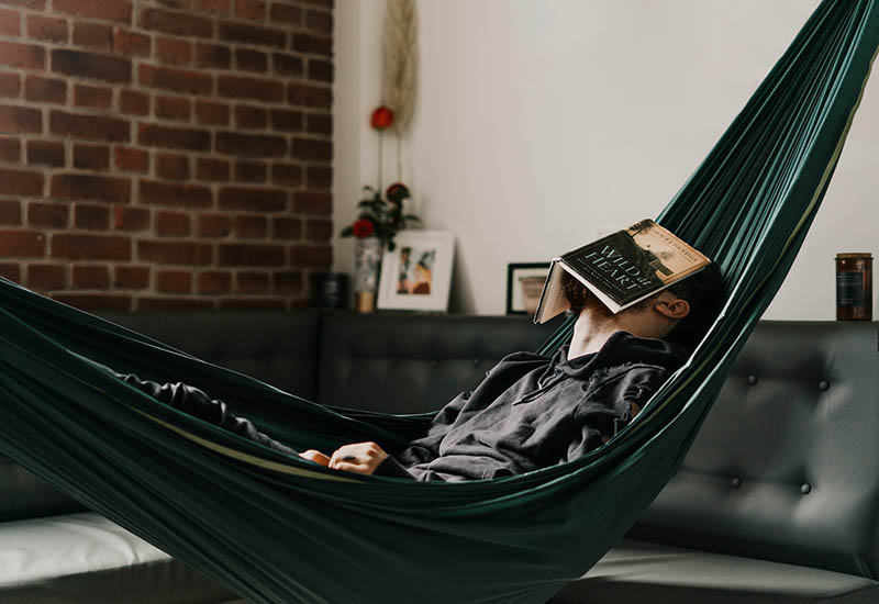man sleeping with book on his face on a hammock indoor