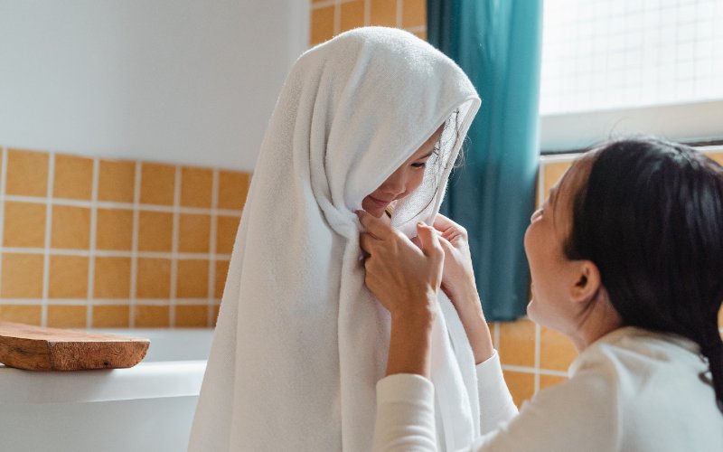 mother drying off child with towel in bathroom
