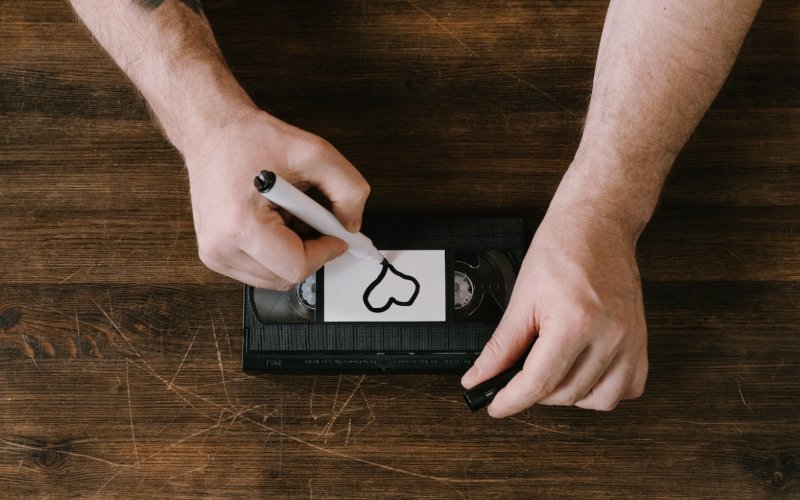 person drawing a heart on the label of a VHS tape