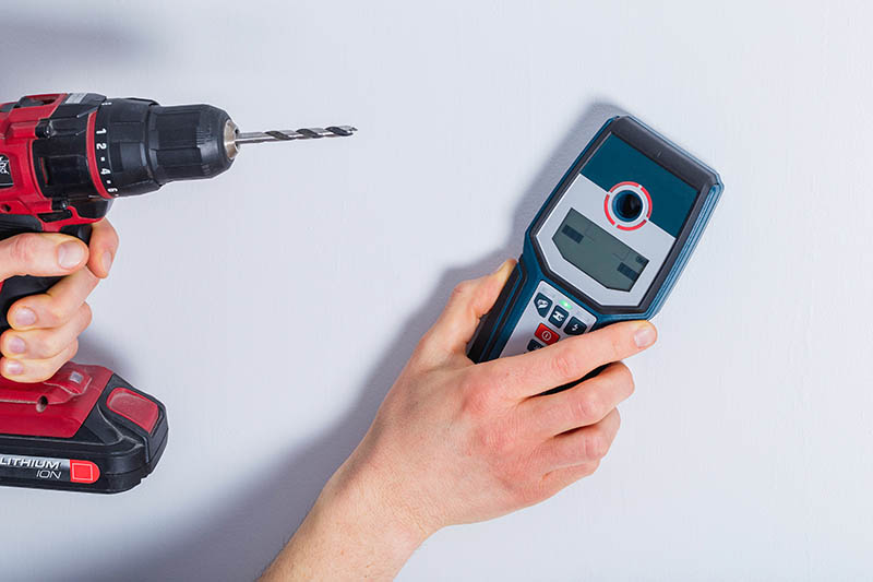 person holding a drill while using stud finder