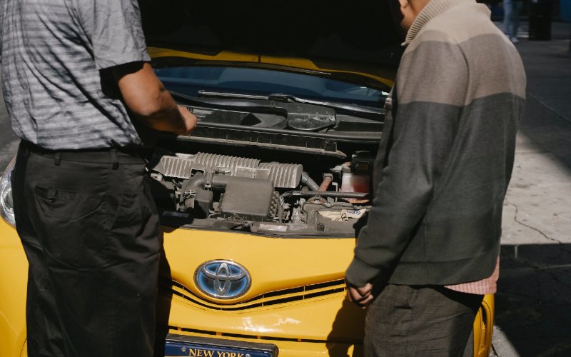 two men standing in front of Toyota car with its hood up