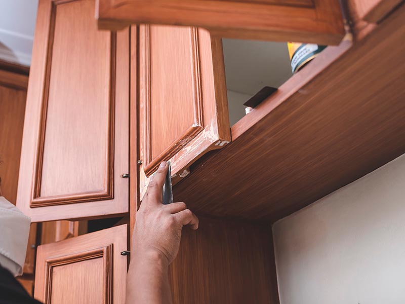 A man sandpapers panels of a wall cabinet filled with wood putty
