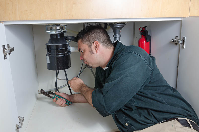 A plumber laying under a house hold sink working on a garbage disposal