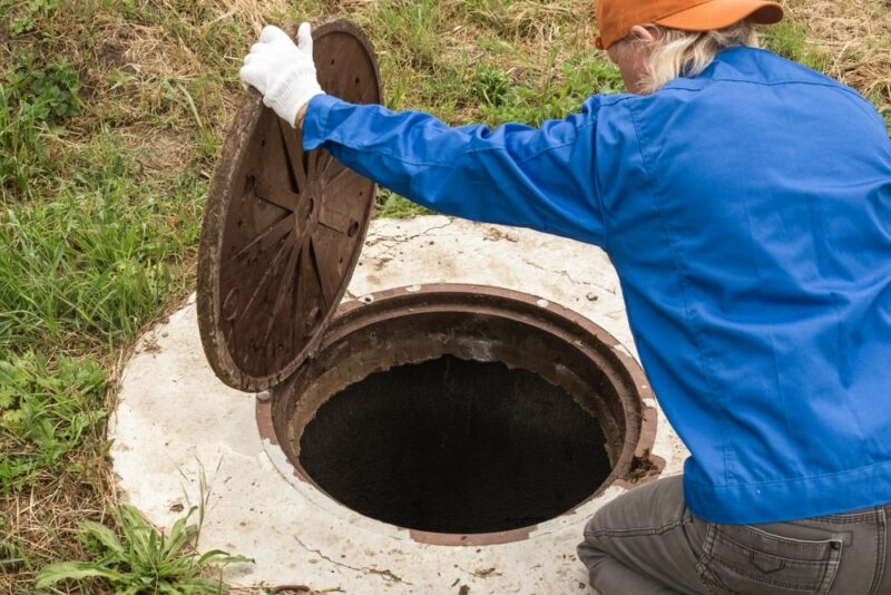A working plumber opens a sewer hatch (cesspool)