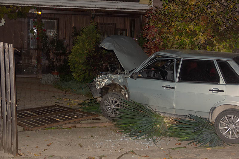 Broken car in the flower bed and a damaged fence in a private home after a night in a car accident