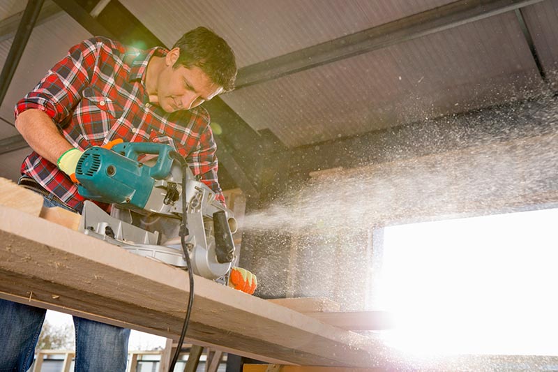 Carpenter cutting wood with circular power saw in building construction site interior