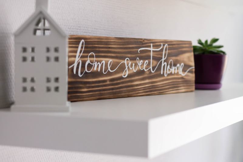 Decorative sign house sweet home sign from a burnt tree on a white shelf with a toy house and a flower pot