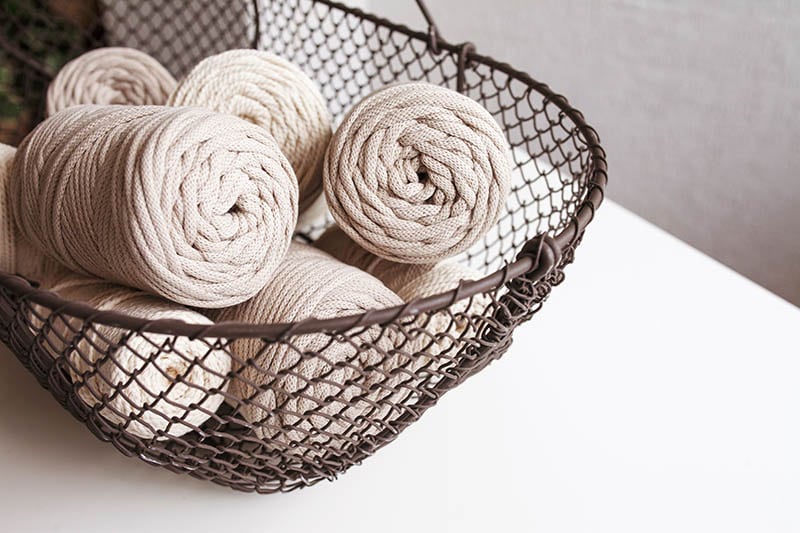 Handmade macrame braiding and cotton threads in basket on white background