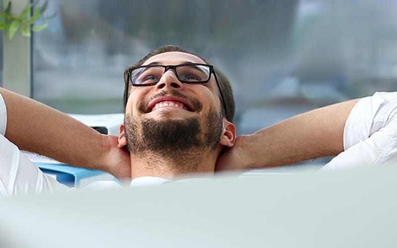 Handsome smiling bearded adult clerk person arms crossed up over head sit behind laptop pc display at office workplace desk