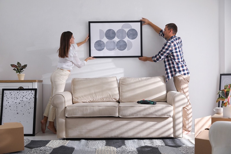 Happy couple hanging picture on white wall together. Interior design