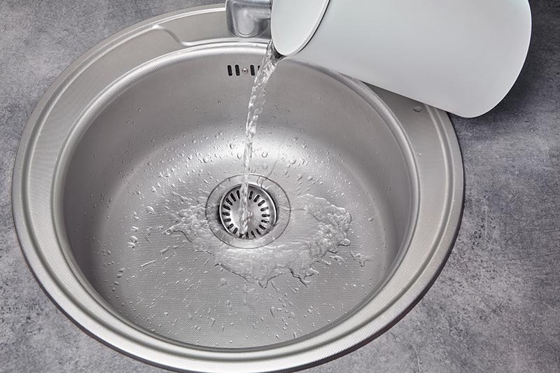 Hot water pours from a white electric kettle into a metal kitchen sink