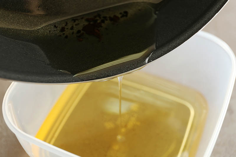 Pouring used cooking oil from frying pan into plastic container