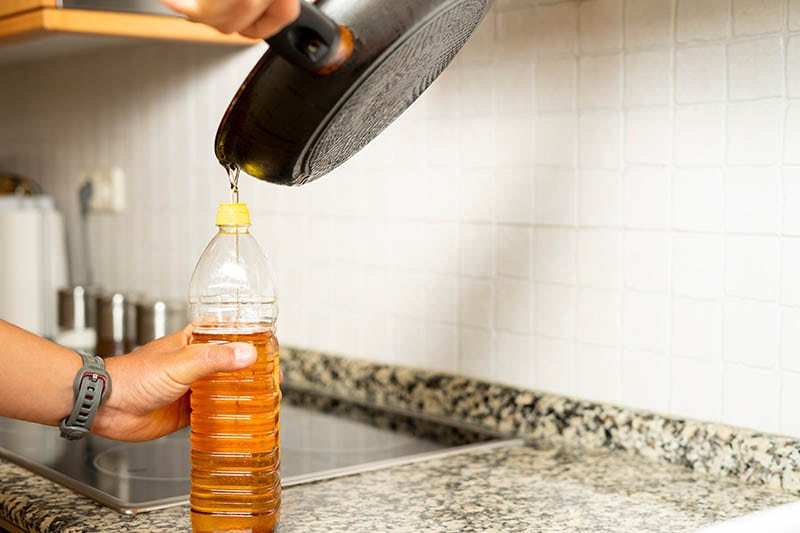 Recycling edible oil from a frying pan into a plastic bottle in his home kitchen