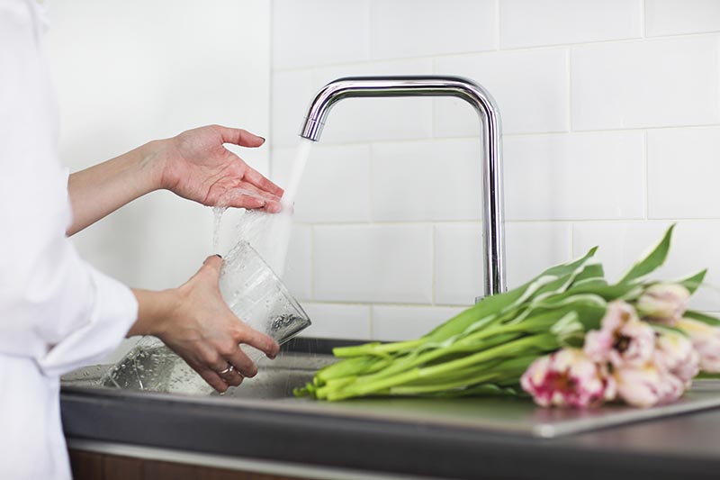 Young woman rinsing and cutting flowers and pouring water into the vase in kitchen sink
