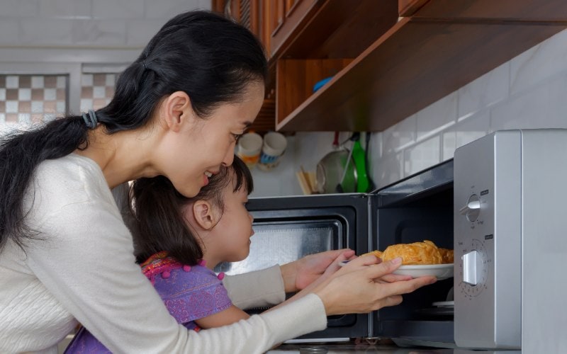a mother assisting her daughter in using the microwave