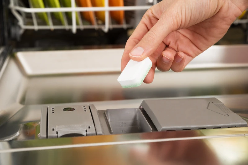 close up of a person putting tablet detergent in dishwasher